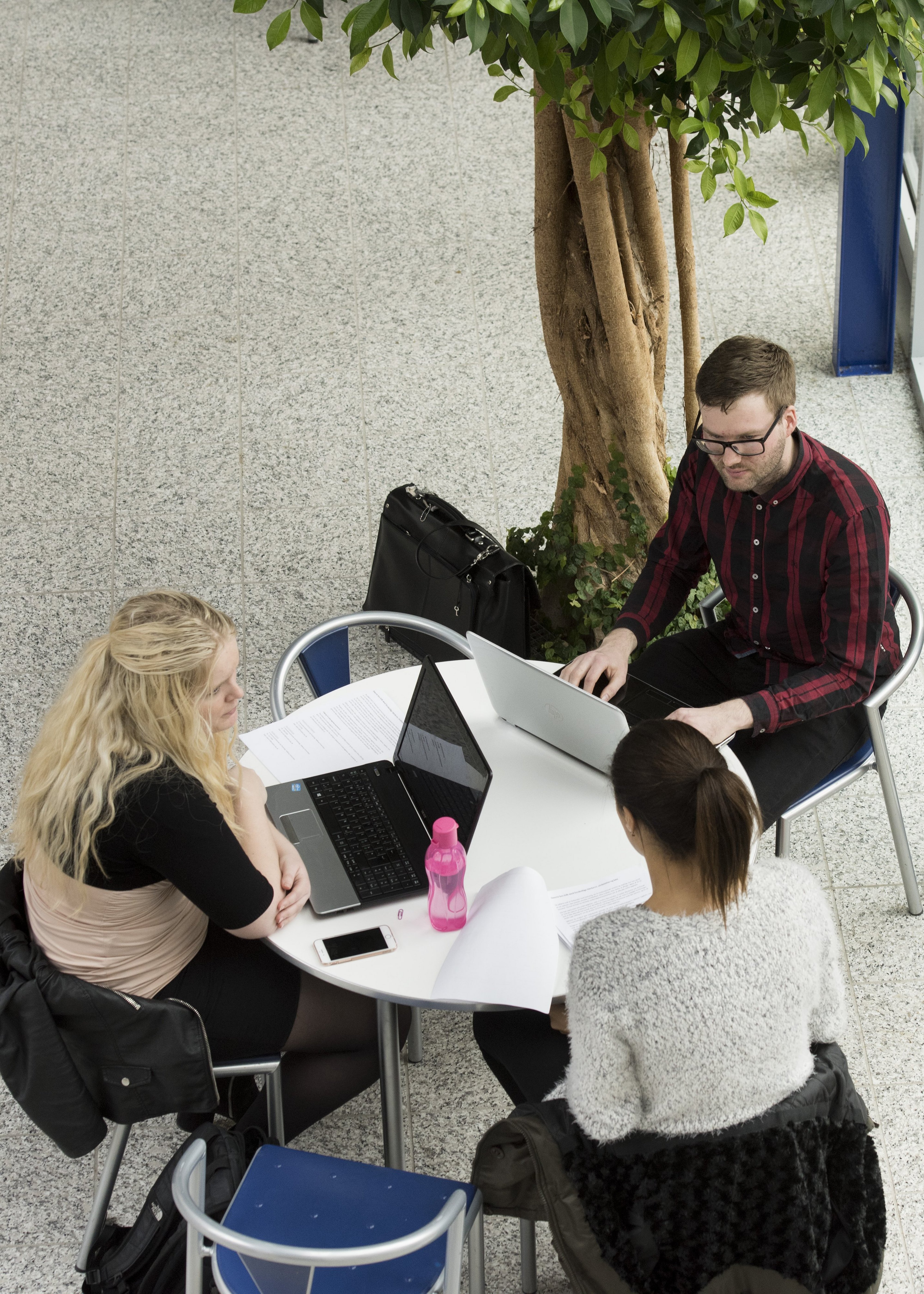 Tre personer sidder ved bord med computere og papirer.