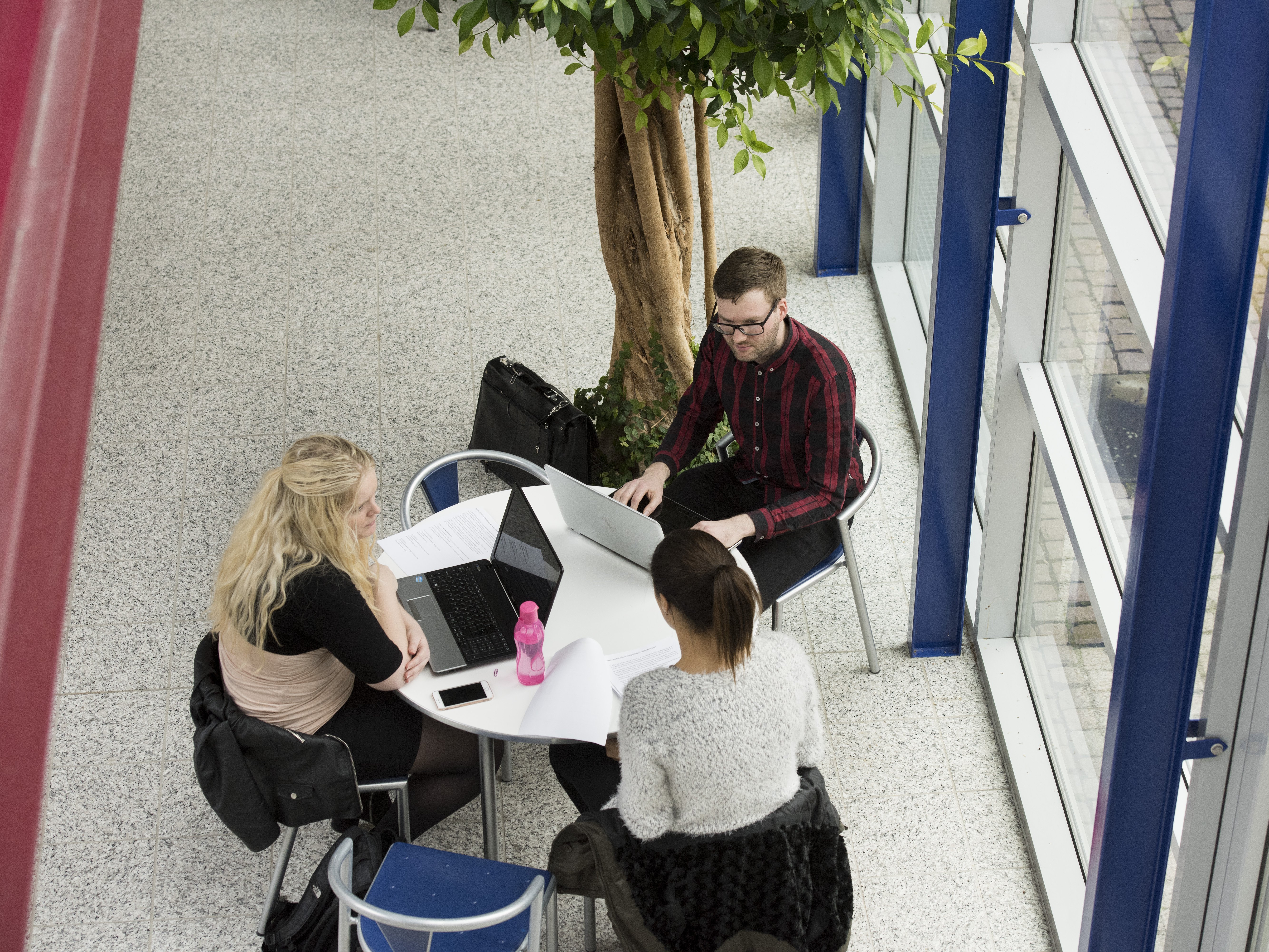 Tre personer sidder ved bord med computere og papirer.